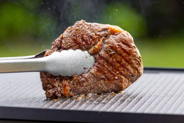 Sıcak elektrikli ızgara yüzeyinde tuzlu ve biberli taze ızgara biftek.