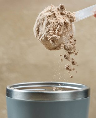Protein tozu, ölçü kaşığından kabın içine dökülür. beyaz spor beslenmesi. Spor ya da diyet içeceği hazırlamak için kuru karışım.