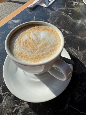 Siyah mermer restoran teras masasında bir fincan kapuçino.