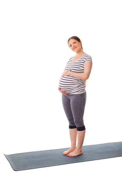 妊娠中笑顔女性立ち上のヨガマット持って彼女の腹絶縁上の白い背景 — ストック写真