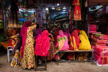Jodhpur, Hindistan - 14 Kasım 2019: Sadar Market 'teki yerel kadınlara yeni örnekler gösteren kumaş satıcısı. Jodhpur, Rajasthan, Hindistan