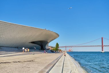 Lizbon, Portekiz - 08 Ağustos 2022: MAAT Sanat, Mimarlık ve Teknoloji Müzesi, Tagus nehrinin kıyısında ve 25 Nisan köprüsünün arka planında uçan uçakla inşa edilen modern bir binadır. Lizbon, Portekiz