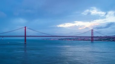 Lizbon 'un ünlü turistik beldesi 25 de Abril Köprüsü' nün Tagus nehri üzerinde Lisboa ve Almada 'yı akşam alacakaranlıkta teknelerle ve hareket eden bulutlarla birleştirmesi. Lizbon, Portekiz. Etkin büyüt