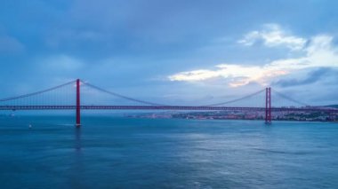 Lizbon 'un ünlü turistik beldesi 25 de Abril Köprüsü' nün Tagus nehri üzerinde Lisboa ve Almada 'yı akşam alacakaranlıkta teknelerle ve hareket eden bulutlarla birleştirmesi. Lizbon, Portekiz
