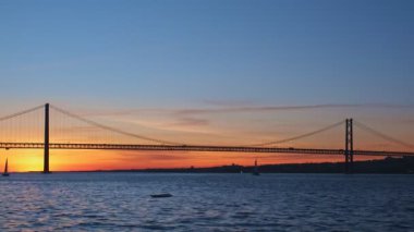 25 de Abril Köprüsü 'nün Tagus nehri üzerinde Setubal Yarımadası' nda Lisboa ve Almada 'yı gün batımında turist yatı silüetiyle birbirine bağlayan ünlü turistik manzarası. Lizbon, Portekiz
