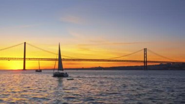 25 de Abril Köprüsü 'nün Tagus nehri üzerinde Setubal Yarımadası' nda Lisboa ve Almada 'yı gün batımında turist yatı silüetiyle birbirine bağlayan ünlü turistik manzarası. Lizbon, Portekiz