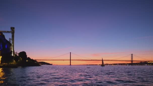 里斯本塔格斯河上著名的里斯本旅游地标 阿布里尔桥25号的景观 日落后与路过的游艇轮廓 还有波卡多文托电梯 葡萄牙里斯本 — 图库视频影像