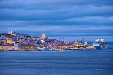 Tagus nehrinin üzerindeki Lizbon manzarasında Almada 'dan gelen feribot akşam alacakaranlıklarında demirli yolcu gemisiyle görülüyor. Lizbon, Portekiz