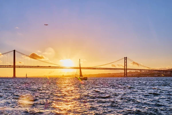 里斯本著名的旅游地标里斯本的25 Abril Bridge连接了塔古斯河上的Setubal半岛上的Lisboa和Almada与日落时的观光游艇轮廓和飞机 葡萄牙里斯本 — 图库照片