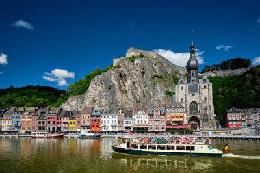 DINANT, BELIGUM - 30 Mayıs 2018: Meuse nehrinin üzerinde turist botuyla Dinant şehri manzarası. Dinant, Belçika 'nın Namur ilinin Meuse Nehri üzerinde yer alan bir Walloon şehridir..