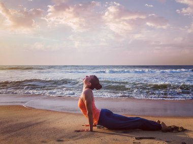Yoga yapan kadın Ashtanga Vinyasa yoga yapıyor Surya Namaskar Sun Salutation asana Urdhva Mukha Svanasana plajda gün batımında köpek pozu veriyor. Vintage retro efekti filtrelenmiş hipster görüntüsü