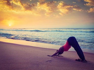 Klasik retro efekt, günbatımında tropikal plajda Yoga 'nın hipster tarzı görüntüsünü filtreledi - Ashtanga Vinyasa yoga yapan kadın Adho mukha svanasana - aşağıya bakan köpek -. Kerala, Hindistan