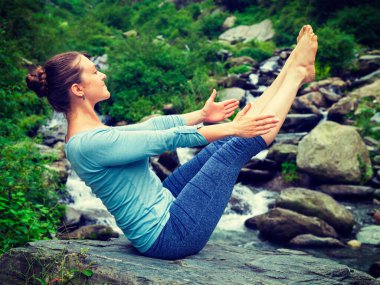 Yoga yapmak için Himalayalar 'da tropikal şelalede Ashtanga Vinyasa asana Navasana pozu veren genç ve sportif bir kadın. Himachal Pradesh, Hindistan. Vintage retro efekti filtrelenmiş sihirbaz.