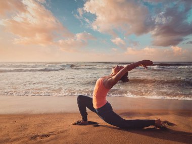 Antika retro efekt filtrelenmiş hippi tarzı yoga görüntüsü - sportif fit kadın Anjaneyasana 'da yoga yapıyor - gün batımında plajda düşük hilal hamlesi pozu