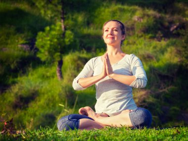 Meditasyon ve açık havada dinlenme yogası - Padmasana Lotus Pozu 'nda meditasyon yapan ve rahatlatan genç bir kadın) ormandaki yeşil çimlerde namaste mudra ile. Vintage retro efekti filtrelenmiş hipster tarzı resim.