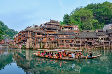 FENGHUANG, CHINA - APRIL 21, 2018: Chinese tourist attraction destination - Feng Huang Ancient Town (Phoenix Ancient Town) on Tuo Jiang River with bridge and tourist boat. Hunan Province, China clipart