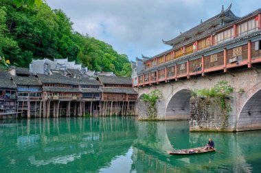 FENGHUANG, ÇİN - 23 Nisan 2018: Feng Huang Antik Kenti 'nde (Phoenix Antik Kenti), Tuo Jiang Nehri' nde, köprüsü ve turist teknesi olan kimliği belirsiz Çinli adam. Hunan Eyaleti, Çin