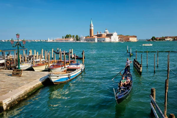 stock image VENICE, ITALY - JULY 19, 2019: Gondolier with tourists in gondola in lagoon of Venice by Saint Mark San Marco square San Giorgio di Maggiore church in Venice, Italy seen from Ponte della Paglia