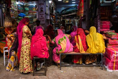 Jodhpur, Hindistan - 14 Kasım 2019: Sadar Market 'teki yerel kadınlara yeni örnekler gösteren kumaş satıcısı. Jodhpur, Rajasthan, Hindistan
