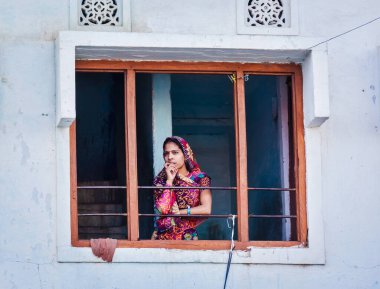 UDAIPUR, INDIA - 24, 2012: Pencerede geleneksel Rajasthani kıyafetli Hintli kadın. Rajasthan 'daki Udaipur başlıca turizm beldelerinden biri.