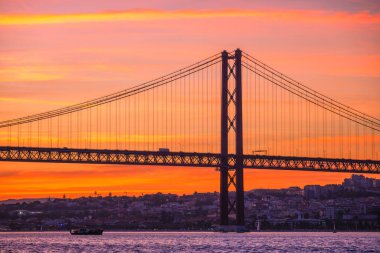 Lizbon 'un ünlü turistik beldesi 25 de Abril Köprüsü' nün Tagus nehri üzerinde Lisboa ve Almada 'yı gün batımında turist botu siluetiyle birbirine bağlayan görüntüsü. Lizbon, Portekiz