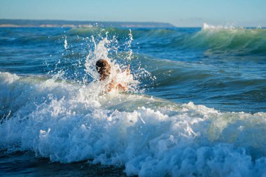 Çocuk Atlantik Okyanusu 'nun okyanus dalgalarında zıplamaktan zevk alıyor. Fonta da Telha plajı, Costa da Caparica, Portekiz
