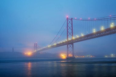 Lizbon 'un ünlü turistik beldesi 25 de Abril Köprüsü' nün Lisboa ve Almada 'yı yoğun sis bulutu altında, altından geçen teknelerle birbirine bağlayan görüntüsü. Lizbon, Portekiz