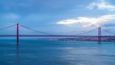 Lizbon 'un ünlü turistik beldesi 25 de Abril Köprüsü' nün Tagus nehri üzerinde Lisboa ve Almada 'yı akşam alacakaranlıkta teknelerle ve hareket eden bulutlarla birleştirmesi. Lizbon, Portekiz. Uzaklaştırma efekti