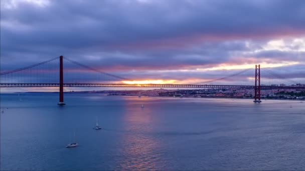 リスボンとアルマダを結ぶリスボンの有名な観光名所である25 Abil Bridgeが日没にタガス川を渡ってセトゥーバル半島で時間が経過しました ポルトガルのリスボン — ストック動画