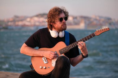 Hipster sokak müzisyeni, günbatımında sette elektro gitar çalıyor.