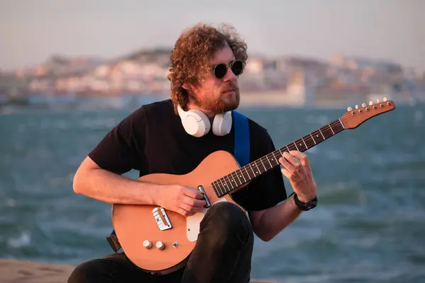 河马街音乐家身穿黑衣 日落时分在路堤上弹奏电吉他 — 图库照片