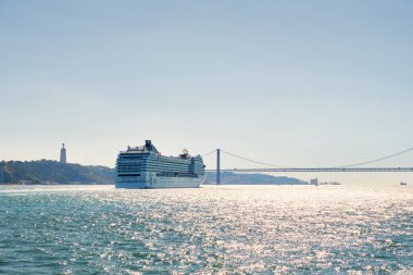 Lizbon, Portekiz - 31 Ağustos 2022: Tagus Nehri 'ndeki Musica sınıfı MSC Orkestra yolcu gemisi ve arka planda 25 de Abril Köprüsü. 1275 kamaraya 2550 yolcu sığdırabiliyordu.