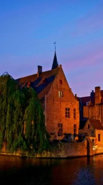 Bruges turistik merkezinin ünlü manzarası - Belfry ile Rozenhoedkaai kanalı ve geceleri ağaçlı kanal boyunca eski evler. Brugge, Belçika. Kamera tavası