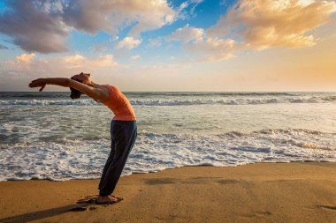 Yoga yapan genç kadın güneş selamı Surya Namaskar güneş batımında Hasta Uttanasana 'ya poz veriyor