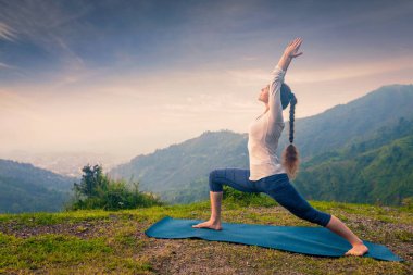 Yoga açık havada - Ashtanga Vinyasa Yoga yapan kadın asana Virabhadrasana 1 Savaşçısı günbatımında HImalayas dağlarında poz veriyor