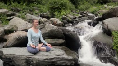 Genç sportif kadın yoga yapıyor - Padmasana 'da meditasyon yapıyor (Lotus Pozu) açık havada tropik şelalede. Himachal Pradesh, Hindistan
