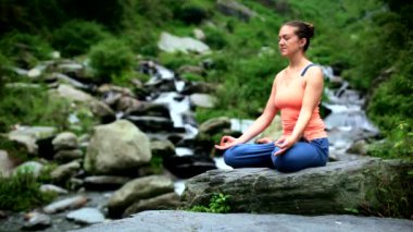 Genç sportif kadın yoga yapıyor - Padmasana 'da meditasyon yapıyor (Lotus Pozu) açık havada tropik şelalede. Himachal Pradesh, Hindistan