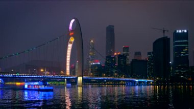 Guangzhou 'nun Zhujiang Nehri üzerindeki Liede Köprüsü manzarası ve finans bölgesinin modern gökdelenleri gece aydınlandı ve köprü altından geçen turist botu görülüyor. Guangzhou, Çin