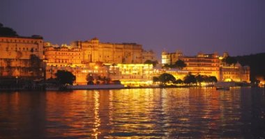 Pichola Gölü kıyısındaki ünlü lüks Udaipur Sarayı, gün batımında su dalgalarıyla aydınlandı. Mewar Hanedanı 'nın Rajput mimarisi. Udaipur, Rajasthan, Hindistan.