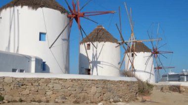 Ünlü Mykonos kasabası yel değirmenlerinin manzarası. Gündoğumunda Mikonos adasındaki geleneksel Yunan yel değirmenleri, arka planda yolcu gemisi Cyclades, Yunanistan. Sabit kamerayla yürüyorum.
