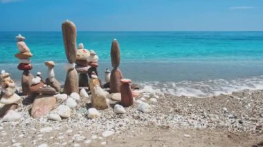 Denge ve uyum kavramı. Doğada mavi denizin sahil kıyısındaki çakıl taşı yığınları. Taş istifleme meditasyon sanatı. Kamera yatay doli takip ediyor. Agia Kiriaki plajı, Milos adası, Yunanistan