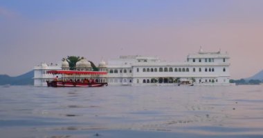 Udaipur Gölü Sarayı 'nın ünlü lüksü Jag Niwa adasında, Pichola Gölü' nde, günbatımında Rajput mimarisi, Mewar Hanedanı 'nın Rajasthan hükümdarlarının mimarisi. Turist botu yan tarafa gidiyor. Udaipur, Hindistan