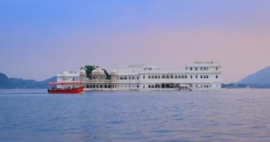 Udaipur Gölü Sarayı 'nın ünlü lüksü Jag Niwa adasında, Pichola Gölü' nde, günbatımında Rajput mimarisi, Mewar Hanedanı 'nın Rajasthan hükümdarlarının mimarisi. Turist botu yan tarafa gidiyor. Udaipur, Hindistan