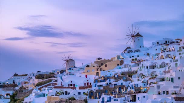 ギリシャの夜の日没にサントリーニ島の伝統的なホワイトハウスと風車を持つ有名なギリシャの象徴的なセルフィースポット観光地オイア村のタイムラプス — ストック動画