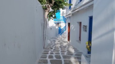 Yunanistan 'ın ünlü Mykonos adasında, Mykonos şehrinin mavi pencereli geleneksel beyaz boyalı evleri ve resimli manzaralı dar caddelerde sabit kameralı bir şekilde yürümek