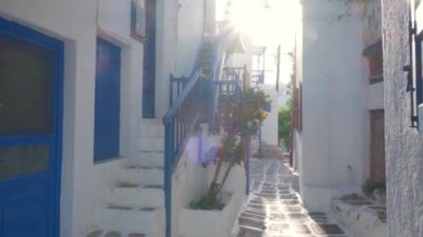 Yunanistan 'ın ünlü Mykonos adasında, Mykonos şehrinin mavi pencereli geleneksel beyaz boyalı evleri ve resimli manzaralı dar caddelerde sabit kameralı bir şekilde yürümek