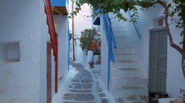 Yunanistan 'ın ünlü Mykonos adasında, Mykonos şehrinin mavi pencereli geleneksel beyaz boyalı evleri ve resimli manzaralı dar caddelerde sabit kameralı bir şekilde yürümek