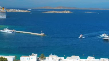 Meşhur yel değirmenleriyle Mykonos kasabası manzarası ve yaz günü tekneleri ve yolcu gemisi olan liman manzarası. Mykonos, Cyclades adaları, Yunanistan. Kamera kaydıyla
