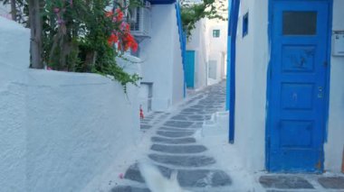 Yunanistan 'ın ünlü Mykonos adasında, Mykonos şehrinin mavi pencereli geleneksel beyaz boyalı evleri ve resimli manzaralı dar caddelerde sabit kameralı bir şekilde yürümek