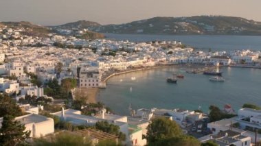 Ünlü yel değirmenleriyle Mykonos kasabası manzarası ve yaz günbatımında tekne ve yatlarla liman manzarası. Mykonos, Cyclades adaları, Yunanistan. Yatay kameralı.